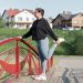 A woman in active wear performs a stretching exercise on a red bridge in a suburban park setting.